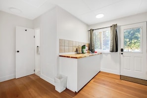 Une pièce avec un plancher en bois, des murs blancs, un pare-feu en carrelage, une fenêtre avec des rideaux et une porte.