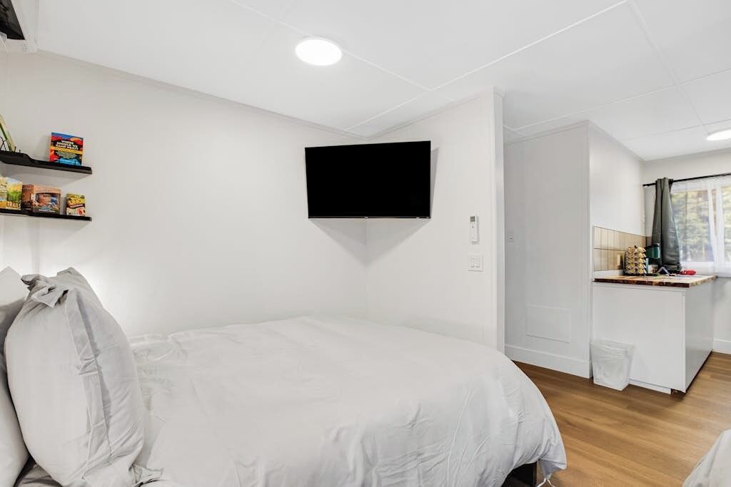 Un dormitorio con cama, televisor montado en la pared y una pequeña zona de kitchenette.