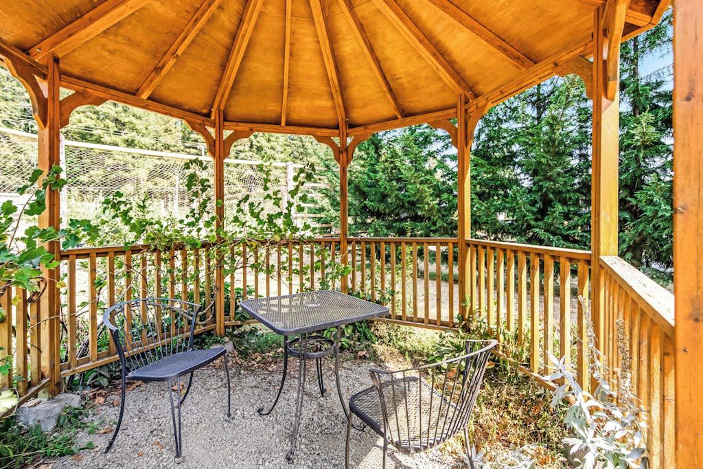 Un belvédère en bois, avec une table et des chaises, entouré d’une clôture en bois et de verdure.