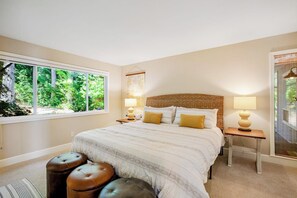 A bedroom with a large bed, two bedside tables, a window with a view of greenery, and a wall-mounted artwork. - Updated 3BR Bayview - Balcony - Firepit (Allyn)
