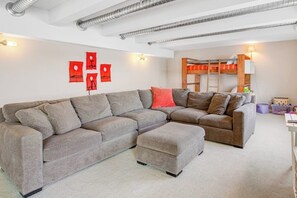 A living room with a sectional sofa, a wooden bunk bed, and a wall-mounted lamp. - Updated 3BR Bayview - Balcony - Firepit (Allyn)