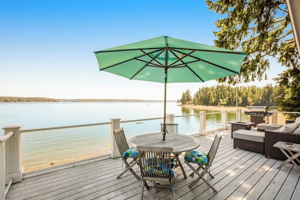 Eine Terrasse mit Tisch, Stühlen, einem Grill und Blick auf einen See.