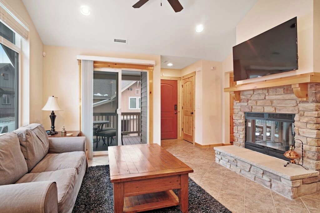 A living room with a sofa, coffee table, fireplace, TV, and a door leading to a balcony.