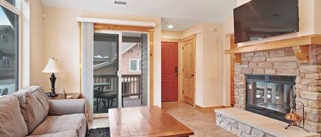 A living room with a sofa, coffee table, fireplace, TV, and a door leading to a balcony.