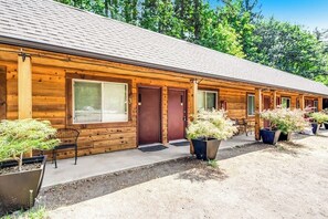 Une rangée de chalets en rondins dotés de grandes fenêtres et de grandes portes, d’un espace extérieur aménagé pour s’asseoir et de plantes en pot.