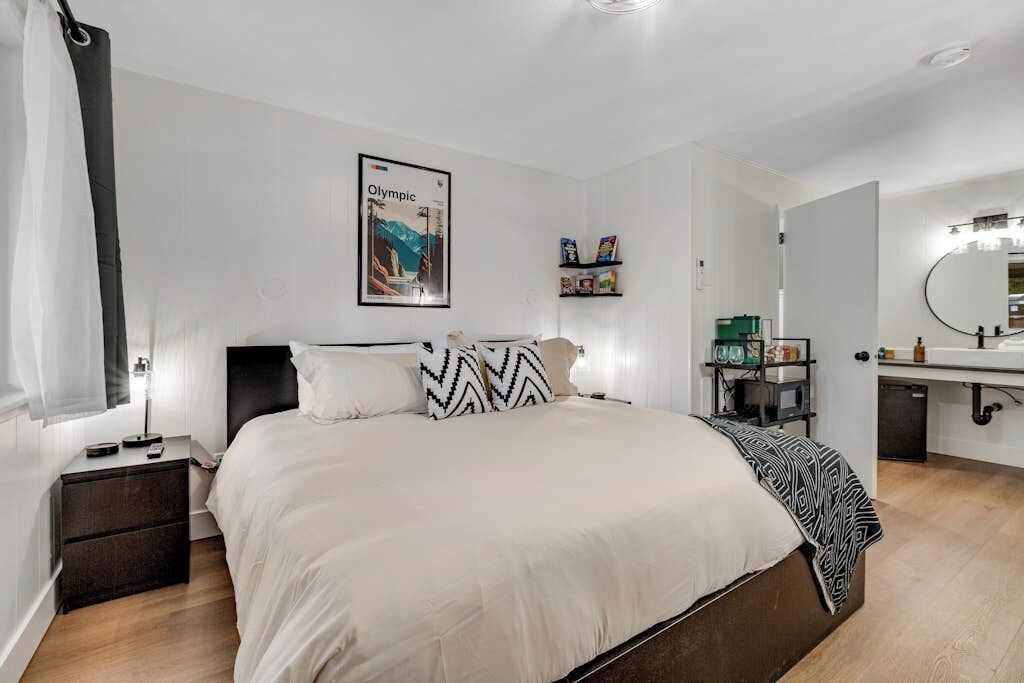 Une chambre à coucher moderne avec un lit, des tables de chevet, une commode, un miroir et une étagère remplie de livres.