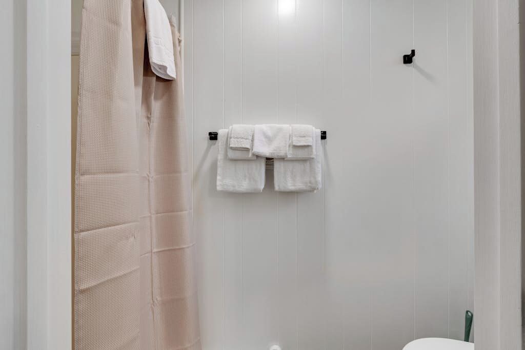Un baño con un toallero que sostiene dos toallas blancas, una cortina de ducha y un inodoro.