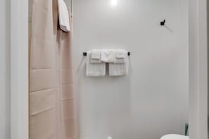 Een badkamer met een handdoekrek met twee witte handdoeken, een douchegordijn en een toilet.