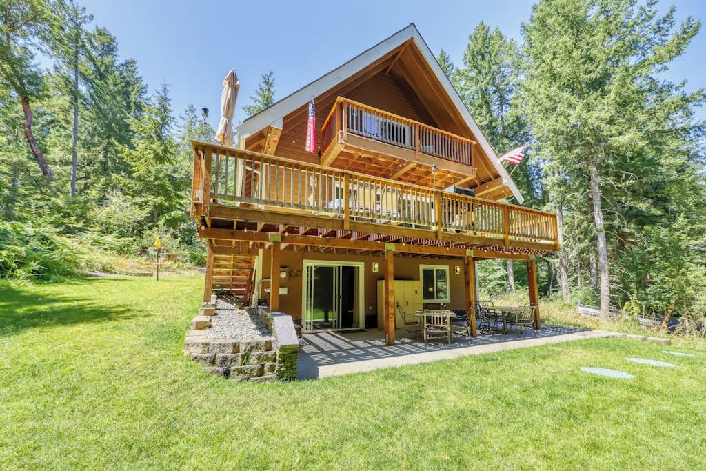 Une cabane en rondins à deux étages, dotée d’un balcon et entourée d’une pelouse et d’arbres.