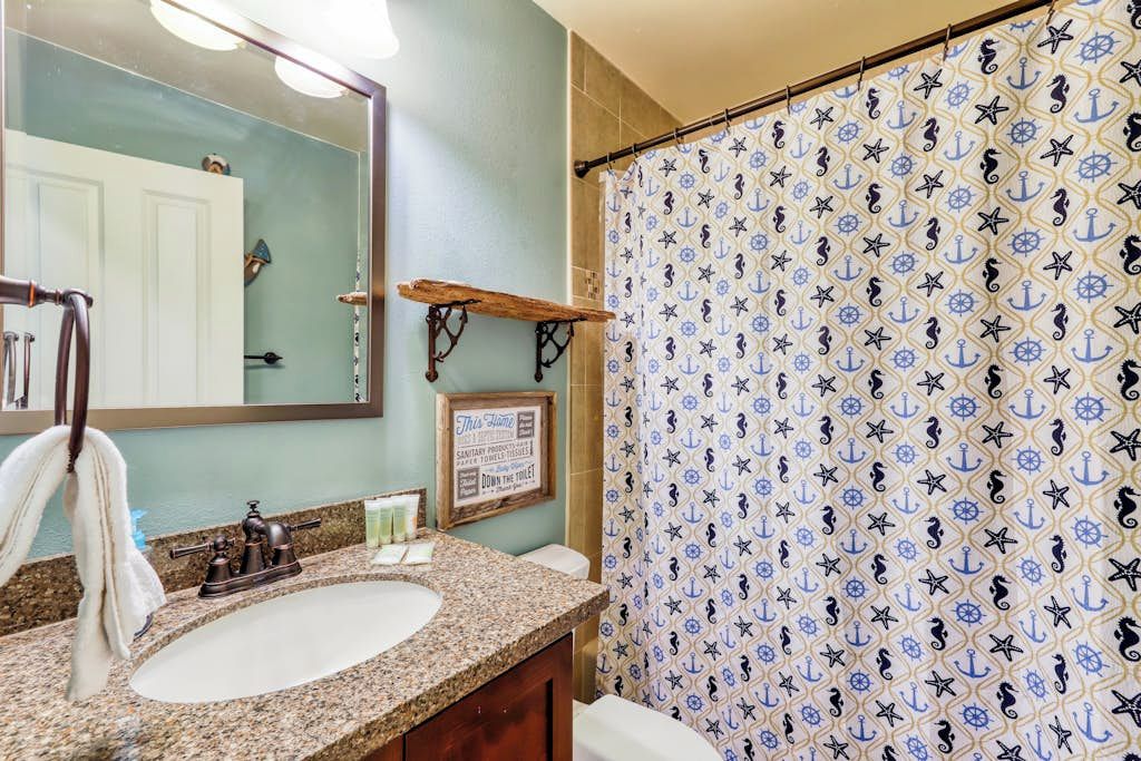 A bathroom with a sink, mirror, and a shower curtain with a nautical pattern.
