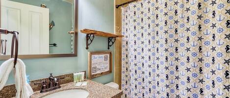 A bathroom with a sink, mirror, and a shower curtain with a nautical pattern.