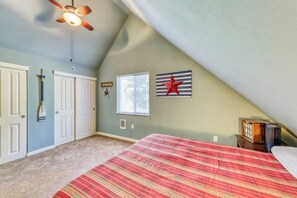 A bedroom with a sloped ceiling, a bed with a striped bedspread, a ceiling fan, a window, and a wall-mounted star decoration.