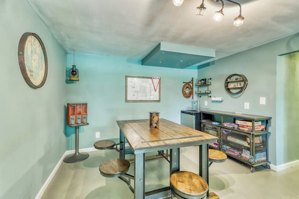 Una habitación con una mesa de madera, taburetes, un mapa en la pared y una estantería con libros.