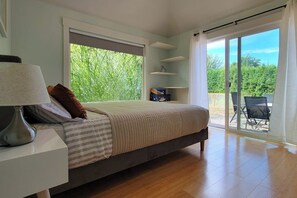 Ein Schlafzimmer mit einem Bett, einem Nachttisch, einer Lampe, einem Fenster und einer Schiebetür zu einem Außenbereich.