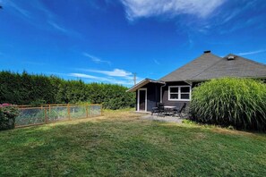 Ein Haus mit dunklem Dach, einem sichtbaren Schornstein und einer kleinen Terrasse mit Gartenmöbeln.