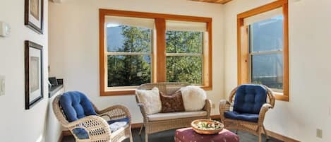 A room with wicker furniture, a patterned rug, and large windows with a view of trees.