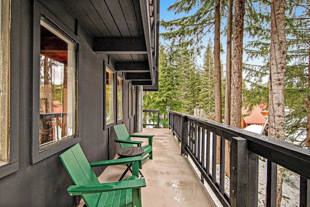 A wooden deck with green chairs and a railing overlooking a forested area.