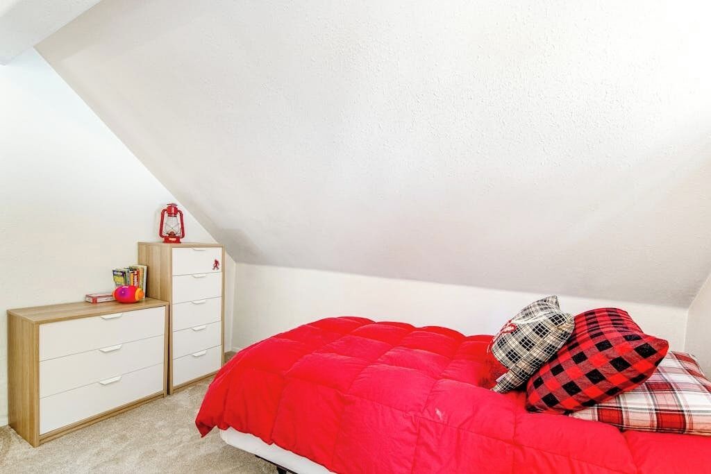 A bedroom with a sloped ceiling, a bed with red bedding, a wooden dresser, and a red lantern.