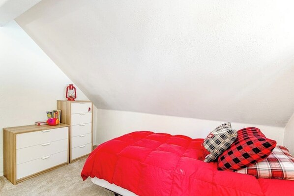 A bedroom with a sloped ceiling, a bed with red bedding, a wooden dresser, and a red lantern. - 4BR - Sauna - WoodStove - Balcony - Firepit - Washer Dryer (Snoqualmie Pass)