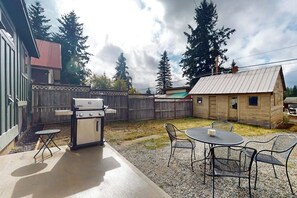 A backyard with a barbecue grill, a small wooden cabin, and a table with chairs. - Cabin 3BR - Foosball - Gas Grill - Kids Games (Ronald)