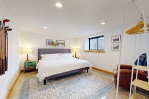 A bedroom with a bed, a nightstand, a lamp, a window, and a coat rack. - Cabin 3BR - Foosball - Gas Grill - Kids Games (Ronald)
