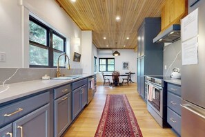 A modern kitchen with grey cabinets, a wooden ceiling, and a red patterned rug. - Cabin 3BR - Foosball - Gas Grill - Kids Games (Ronald)