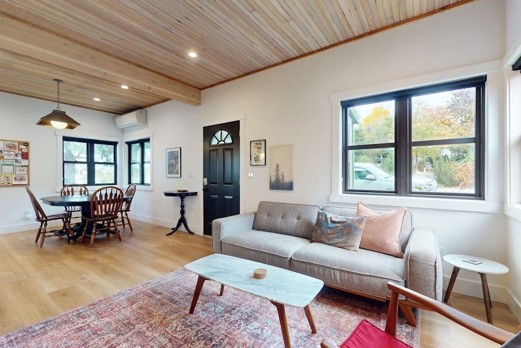 A spacious living room with a wooden ceiling, a sofa, a coffee table, and a dining area with chairs.