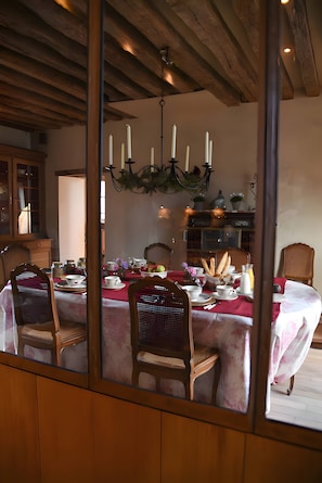 Ein Esszimmer mit Holzbalkendecke, einem Kronleuchter und einem für eine Mahlzeit gedecktem Tisch.