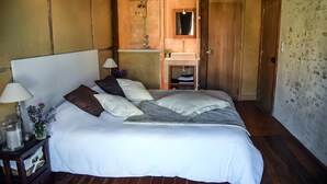 A bedroom with a large bed, a nightstand with a lamp, a small table with a vase of flowers, and a wooden door.