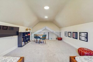 A room with a sloped ceiling, a bookshelf, a table with chairs, a red ottoman, and framed pictures on the wall. - 3 BR Home with loft, game room, fire table & trails (Cle Elum)