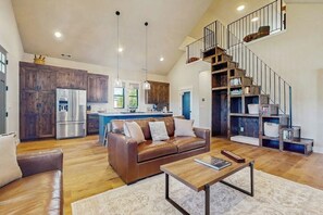 A spacious living area with a brown leather sofa, a wooden coffee table, and a staircase leading to a loft. - 3 BR Home with loft, game room, fire table & trails (Cle Elum)