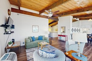 A living room with a ceiling fan, a green sofa, a wooden coffee table, and a blue armchair. - 4BR Bayview - Gas Fire Pit - Balcony - Washer Dryer (Bainbridge Island)