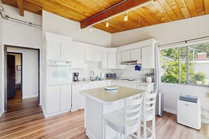 A modern kitchen with white cabinets, a central island, and a large window. - 4BR Bayview - Gas Fire Pit - Balcony - Washer Dryer (Bainbridge Island)