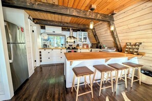 A kitchen with a wooden island, bar stools, a stainless steel refrigerator, and white cabinetry. - Rare cabin with deck, fire pit (Ronald)