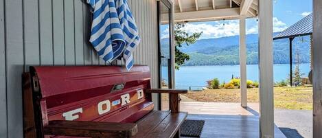 Un espace extérieur abrité, doté d’un banc et d’un barbecue, offrant une vue sur un lac et des montagnes.