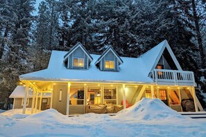 En stuga med en inglasad veranda och en terrass, omgiven av snö och träd.