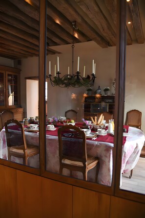Ein Esszimmer mit Holzbalkendecke, einem Kronleuchter und einem für eine Mahlzeit gedecktem Tisch.