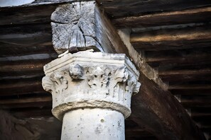 A close-up of a stone column with carved foliage and a capital with a leaf design, part of a building's architecture.