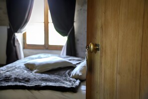 A bedroom with a bed, a wooden door, and a window with curtains.