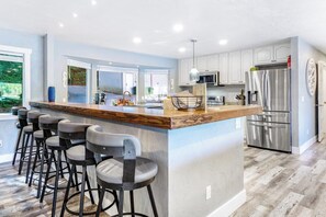 A modern kitchen with a central island, bar stools, stainless steel appliances, and a view of the outdoors. - 4BR Waterview Dog Friendly - Hot Tub - Deck (Union)