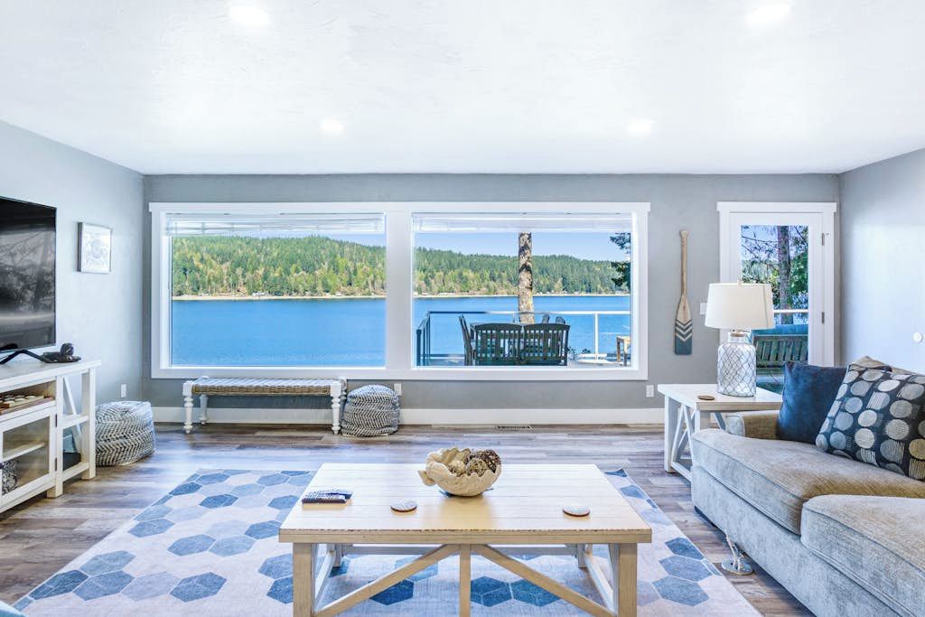 A living room with a large window overlooking a lake, a sofa, a coffee table, and a TV.