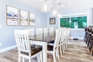 A dining area with a long table and chairs, a clock on the wall, and a window with a view of greenery. - 4BR Waterview Dog Friendly - Hot Tub - Deck (Union)