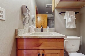 Un baño con lavamanos de mármol, armarios de madera, inodoro blanco, secador de pelo y toallero.