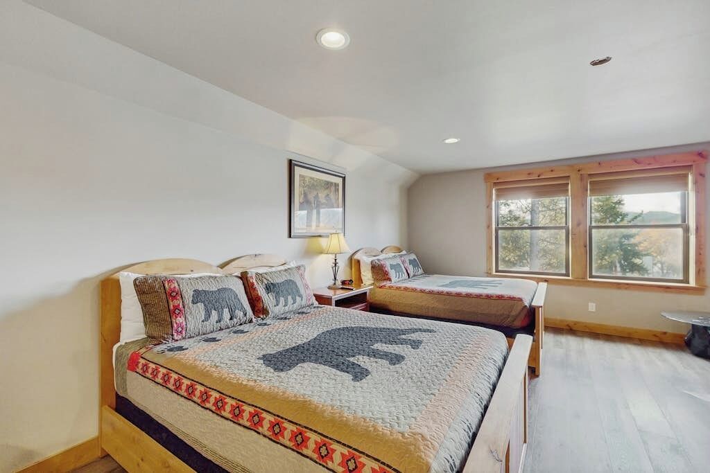 A bedroom with two beds, a window, and a painting on the wall.