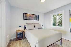 A bedroom with a bed, a nightstand, a lamp, a window with a view of trees, and a painting on the wall. - 1 BR home with private hot tub and dog friendly (Kingston)