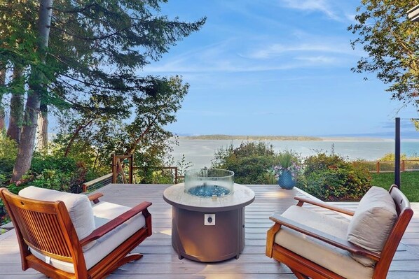 A deck with two wooden lounge chairs and a glass-top fire pit.