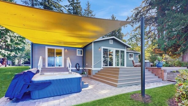 Una casa moderna con un jacuzzi, un porche cubierto y una escalera que lleva a la entrada.