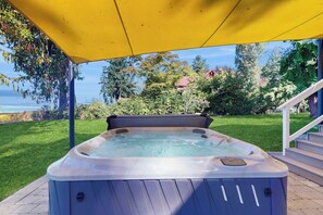 Un jacuzzi bajo un toldo amarillo en un patio trasero con vista a una casa y árboles.