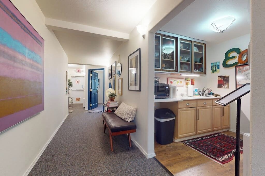 A hallway with a bench, a trash bin, and a kitchen area with cabinets and a microwave.
