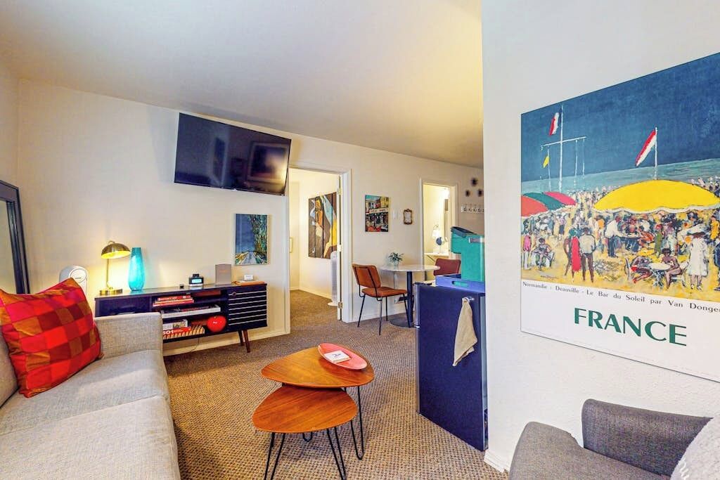 A living room with a sofa, coffee table, TV, and a poster of a beach scene.